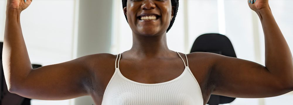 Woman in sports attire flexing both arms at gym 