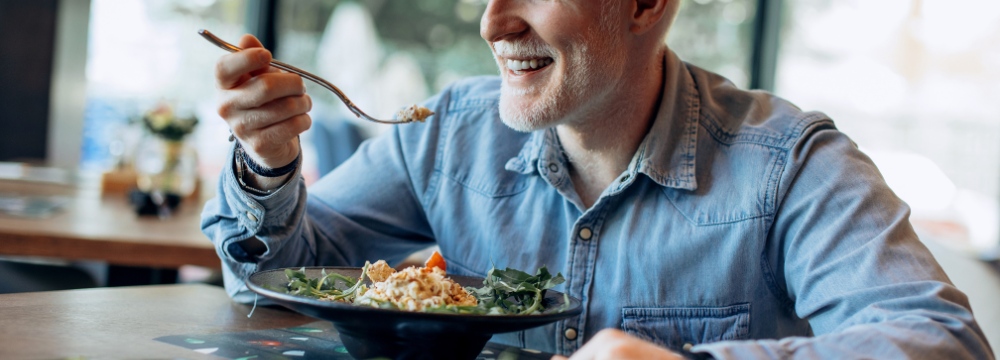 Man eating out of bowl at restaurant while smiling lifting fork to mouth 