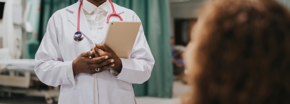 Woman in post-op room talking to physician with hands folded on chest holding clipboard 